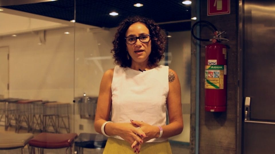 Maria Carolina Trevisan de pé e dando entrevista para o Geledés