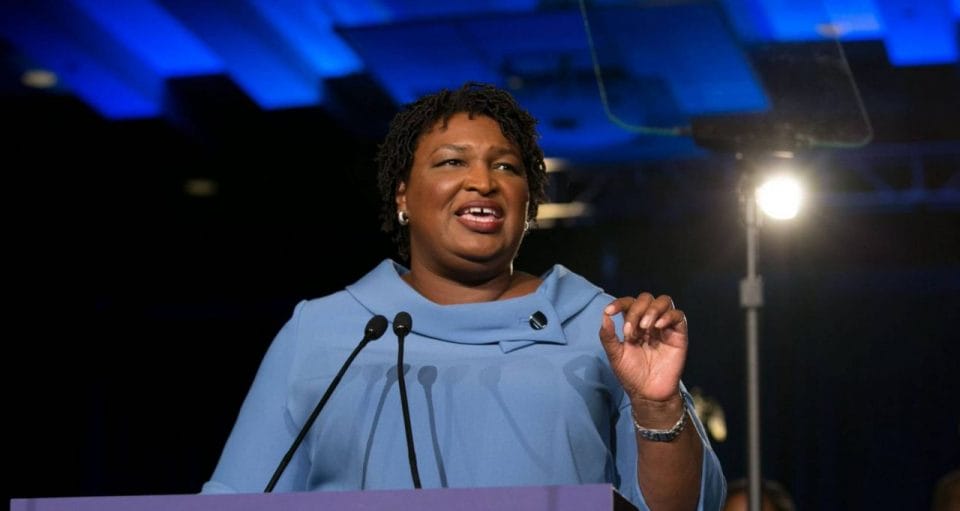 Stacey Abrams de vestido azul discursando ao microfone