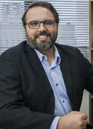 Daniel Cara sentado de terno azul e sorrindo