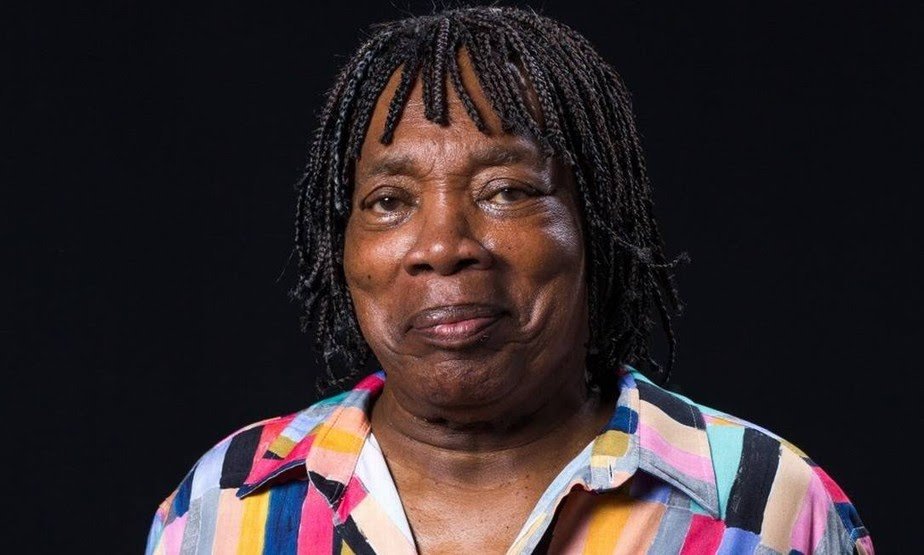 Milton Nascimento- homem idoso negro, de tranças, usa camiseta colorindo- em pé olhando para frente