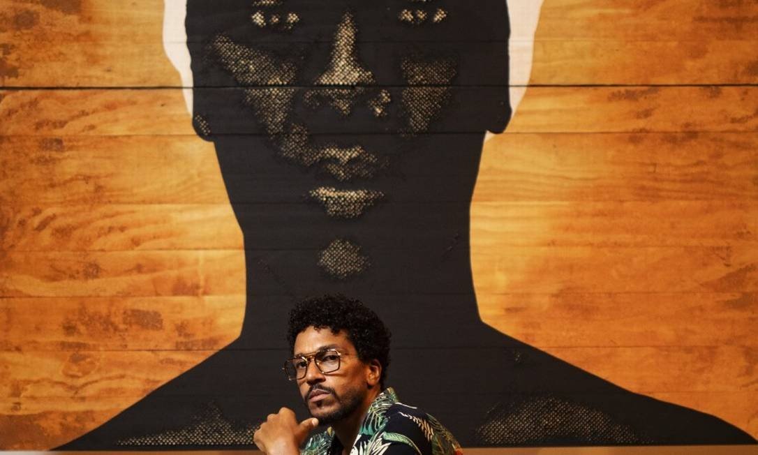 O artista Alexis Peskine - homem negro, usando óculos e camista colorida- agachado no chão